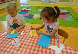 Dzieci naklejają żółty papier na kartkę.